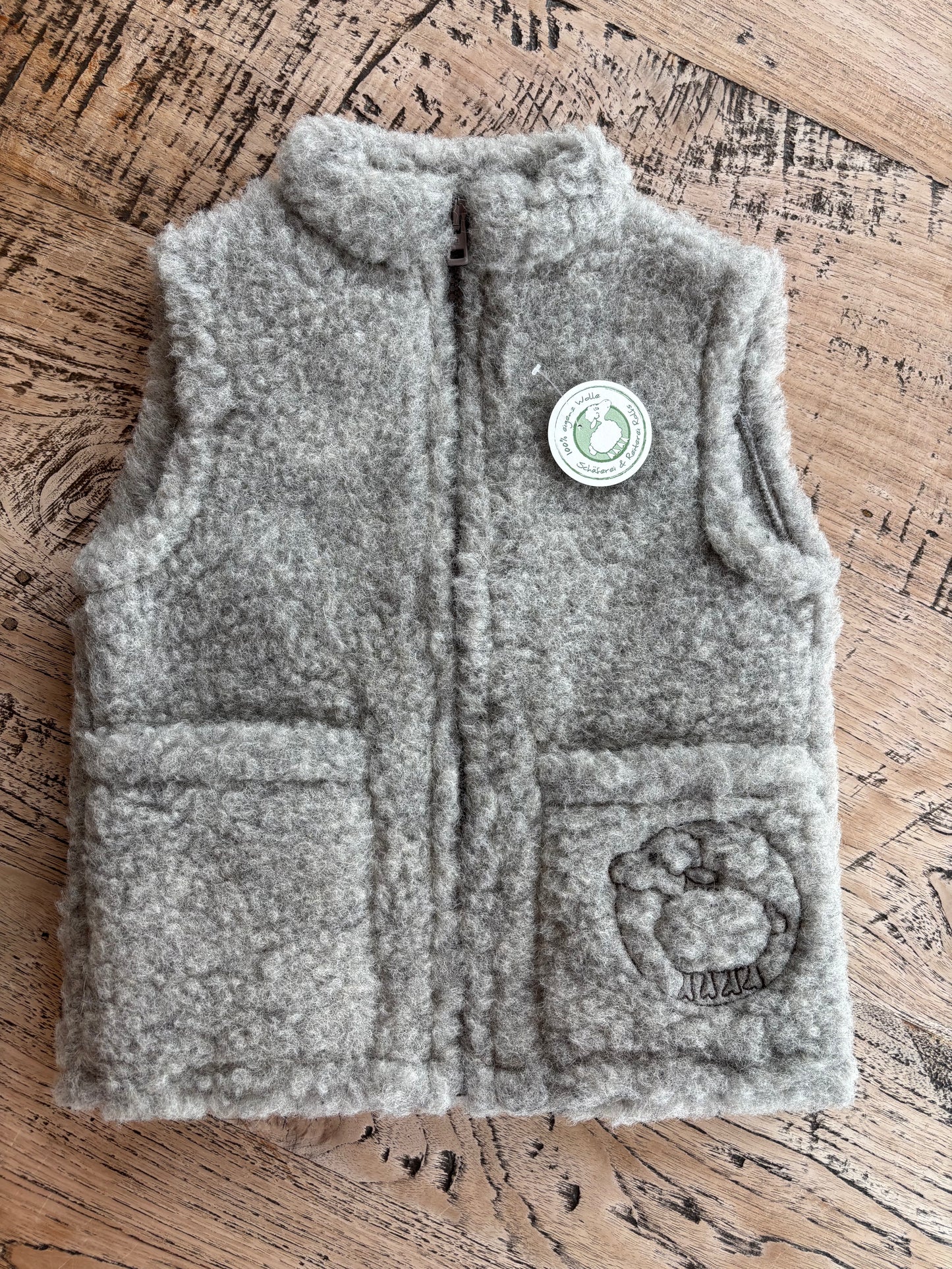 Graue Kinderweste aus reiner Schurwolle, liegend fotografiert – natürliche Wollstruktur und hochwertige Verarbeitung, produziert in Deutschland bei der Schäferei Rolfs an der Nordsee. Nachhaltig, robust und ideal für aktive Kinder im Alltag.