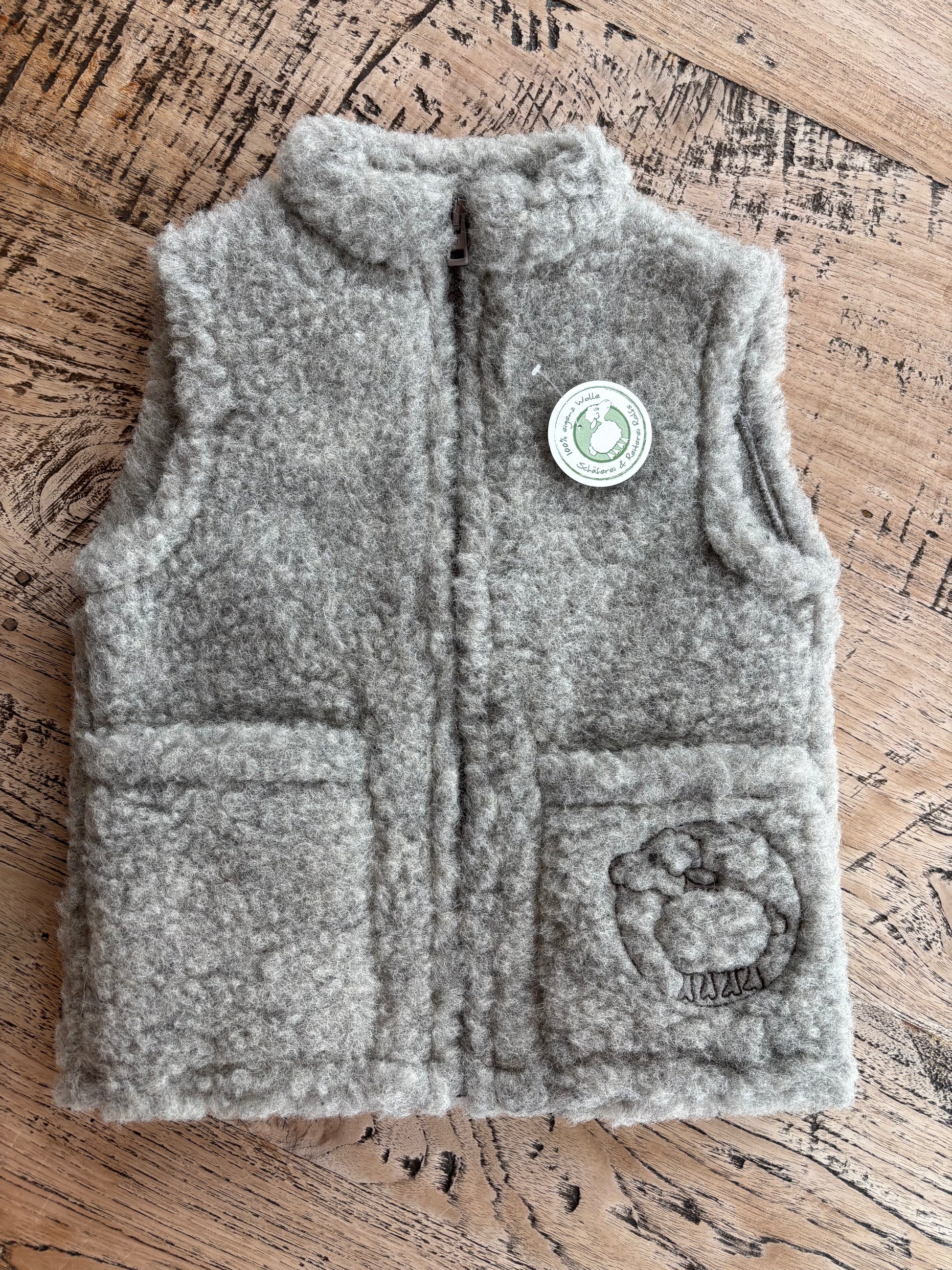 Graue Kinderweste aus reiner Schurwolle, liegend fotografiert – natürliche Wollstruktur und hochwertige Verarbeitung, produziert in Deutschland bei der Schäferei Rolfs an der Nordsee. Nachhaltig, robust und ideal für aktive Kinder im Alltag.