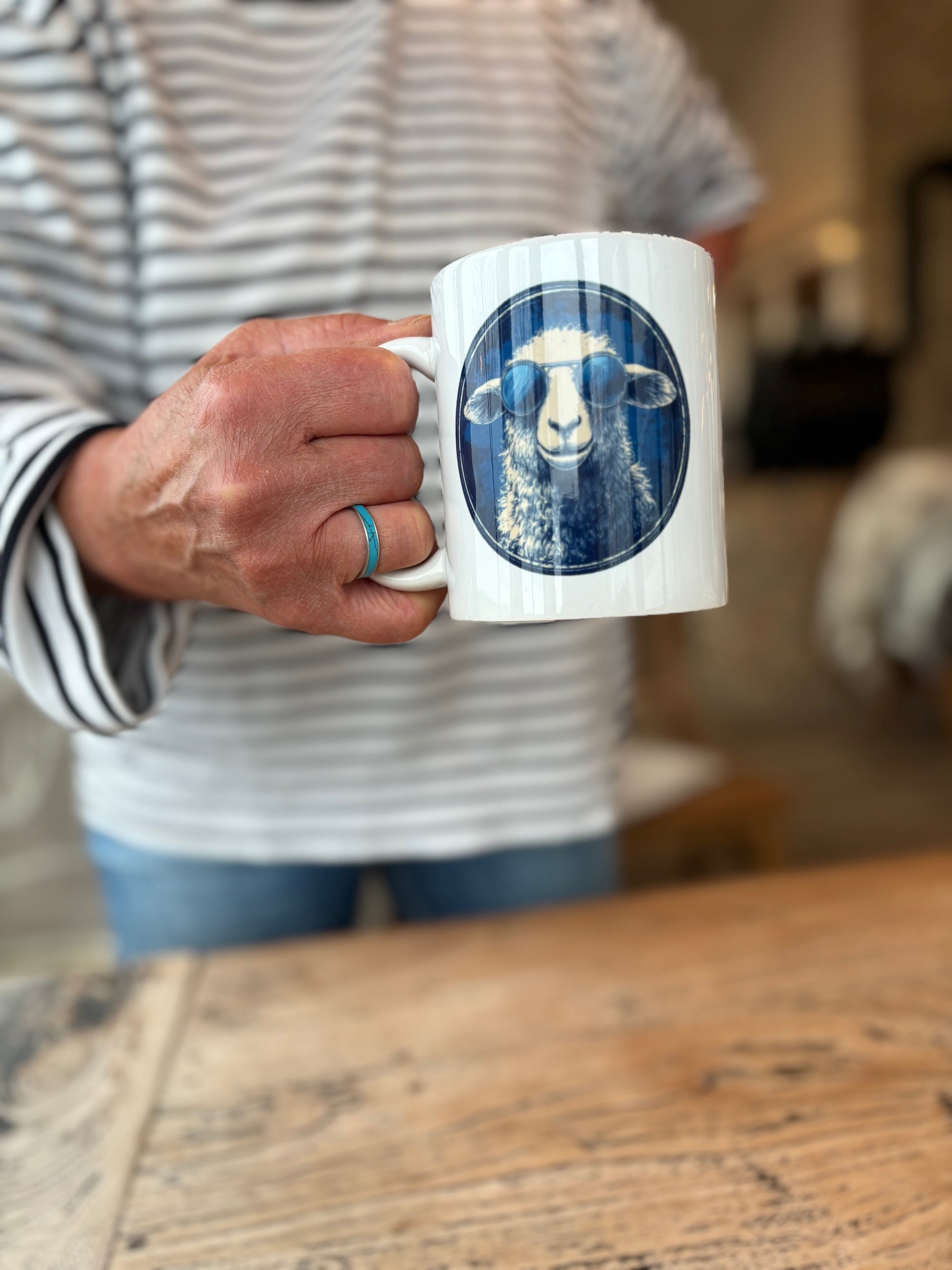 Weißer Porzellanbecher mit blauem Schafmotiv aus der DeichHeld-Kollektion der Schäferei Rolfs an der Nordsee – perfekt für Fans der Schäferei und echte Deichhelden.