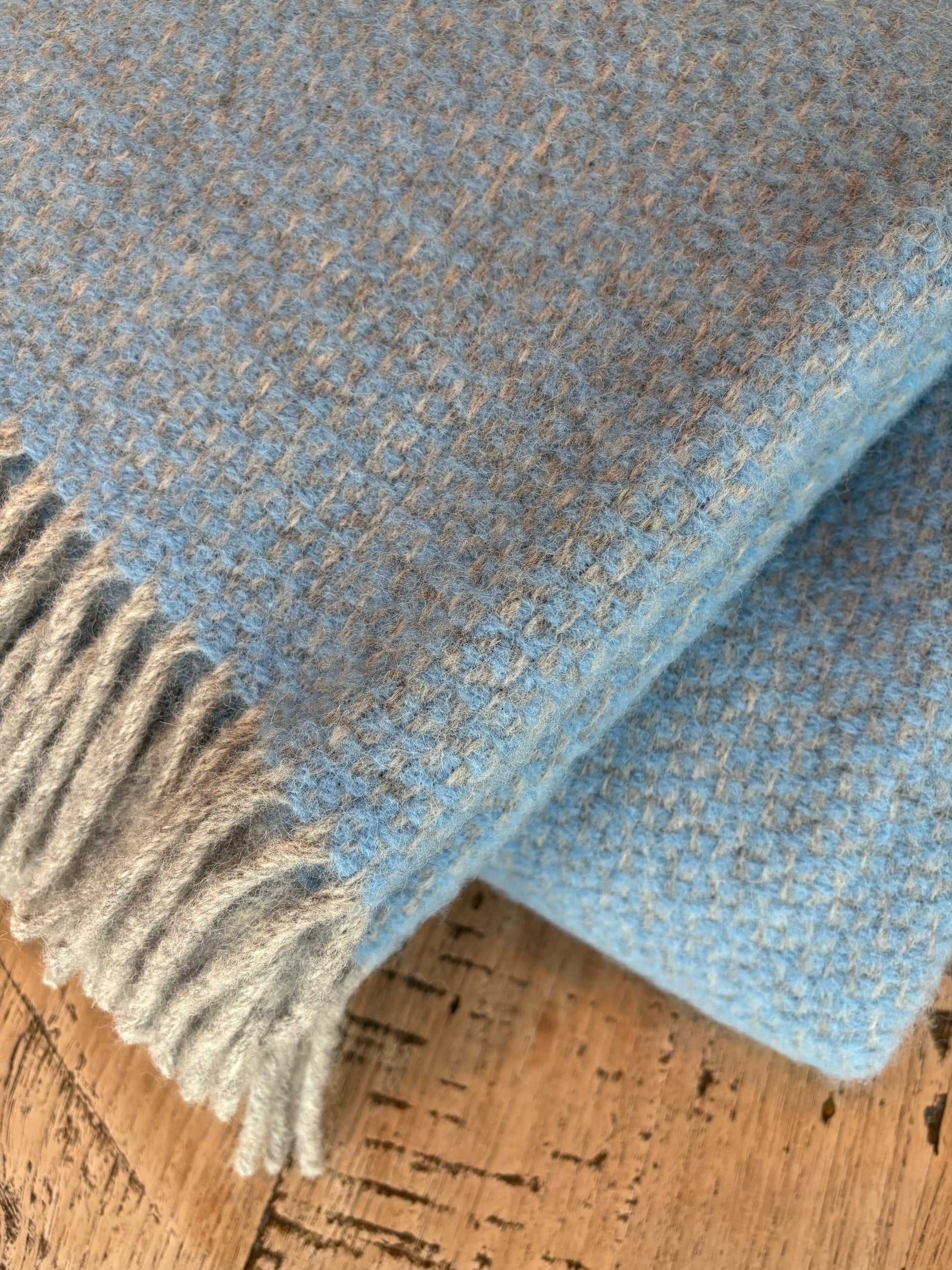Wolldecke „Himmel oder Graublau?“ aus 100 % Schurwolle – zweifarbig gewebt mit feiner Körnung und Fransen. Weich, warm und langlebig wie die Nordsee selbst. Das Lieblingsstück aus der Schäferei Rolfs: hochwertig, natürlich und perfekt zum Einkuscheln auf Sofa oder Bett.